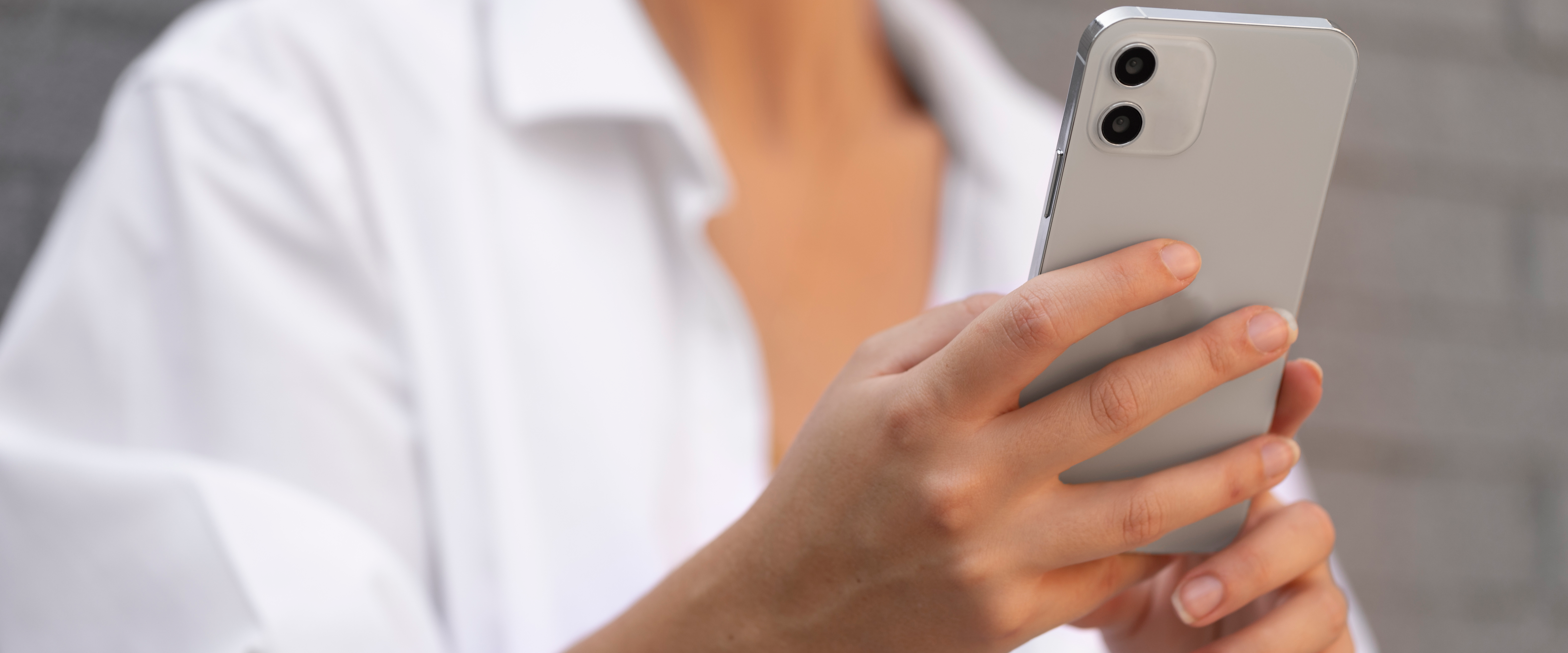 Close up photo of a woman wearing a white blouse holding a smartphone.