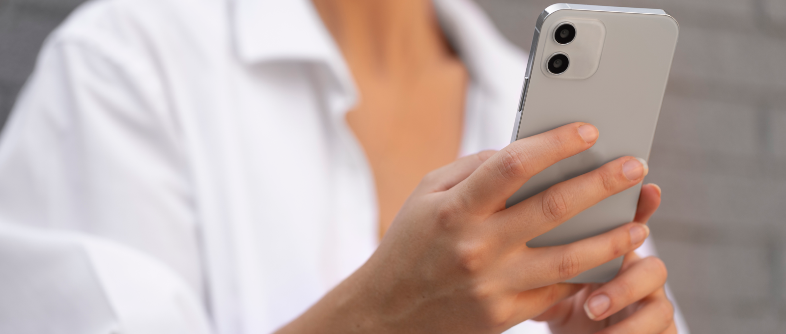 Close up photo of a woman wearing a white blouse holding a smartphone.