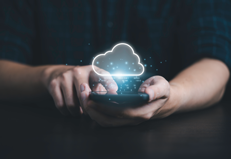 Close up photo of someone holding a smartphone towards the camera in both hands. 'Cloud' and 'IT' graphics have been added floating above the screen.