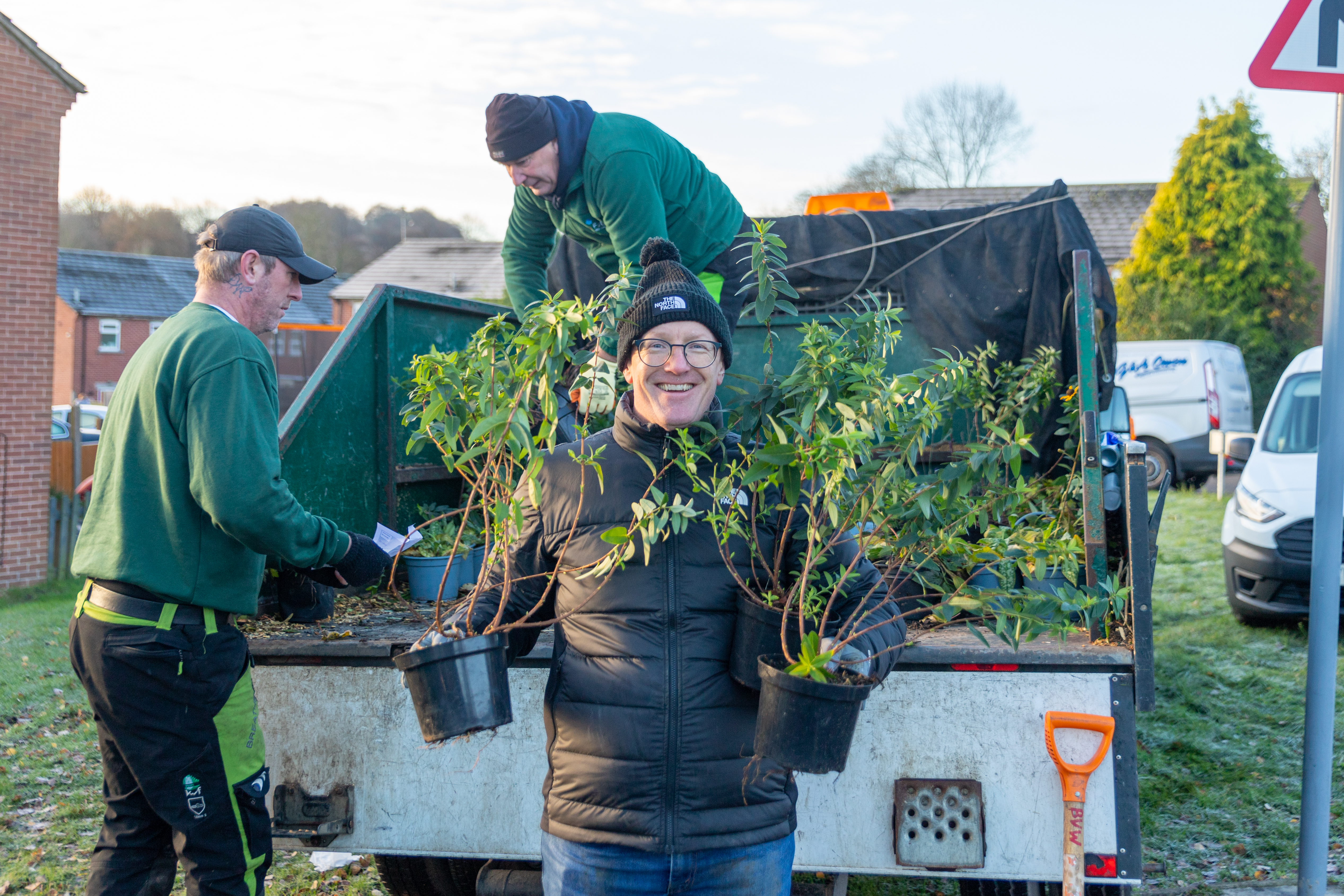 Photo of a Futures employee holding two plants and smiling at the camera as he helps to unload a truck