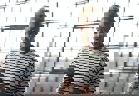 Photo of a young black woman with bleached hair looking at her phone. She is standing in front of a large window.