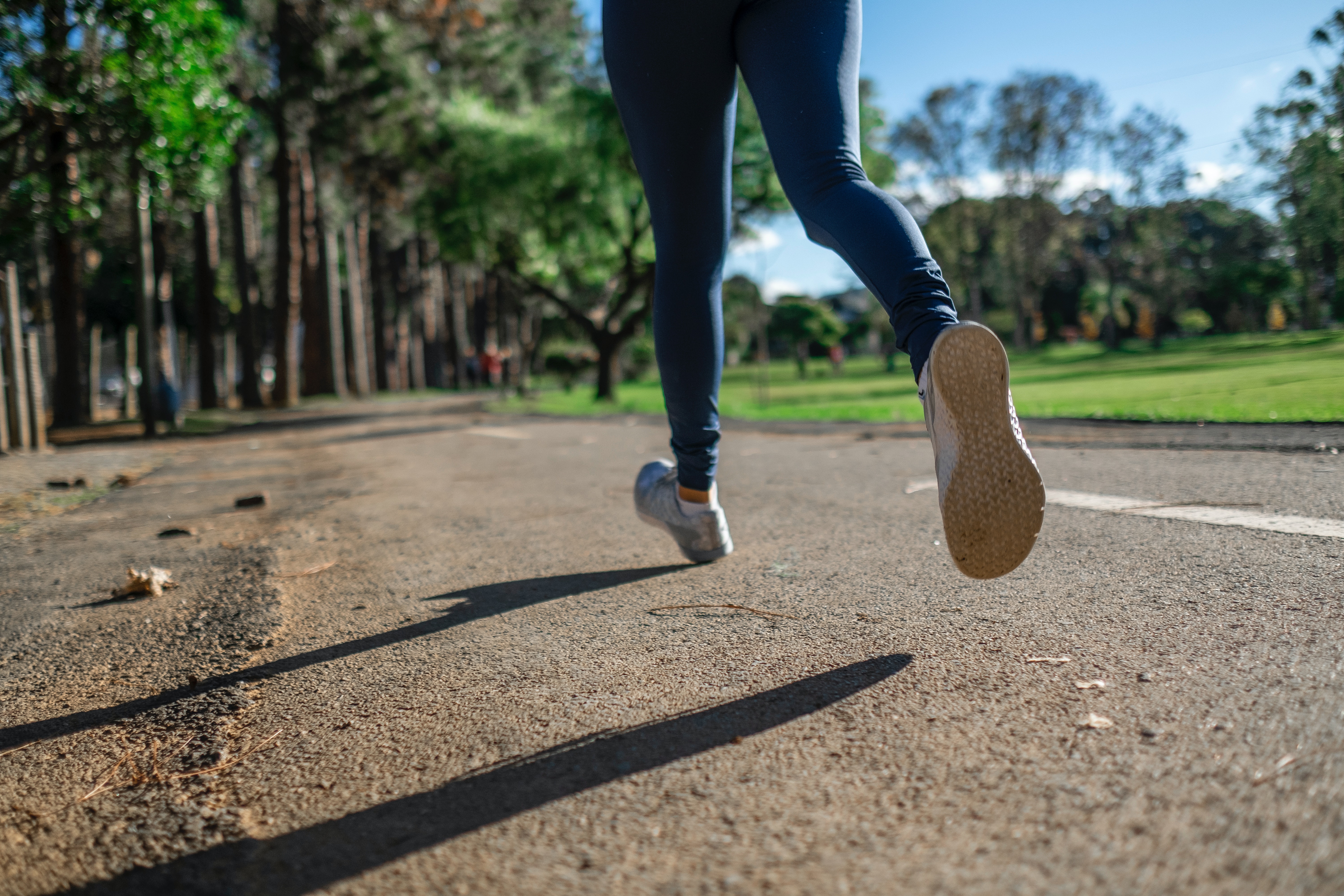 Close up photo of a woman's lower legs and feet taken as she jogs along a pathway in a park