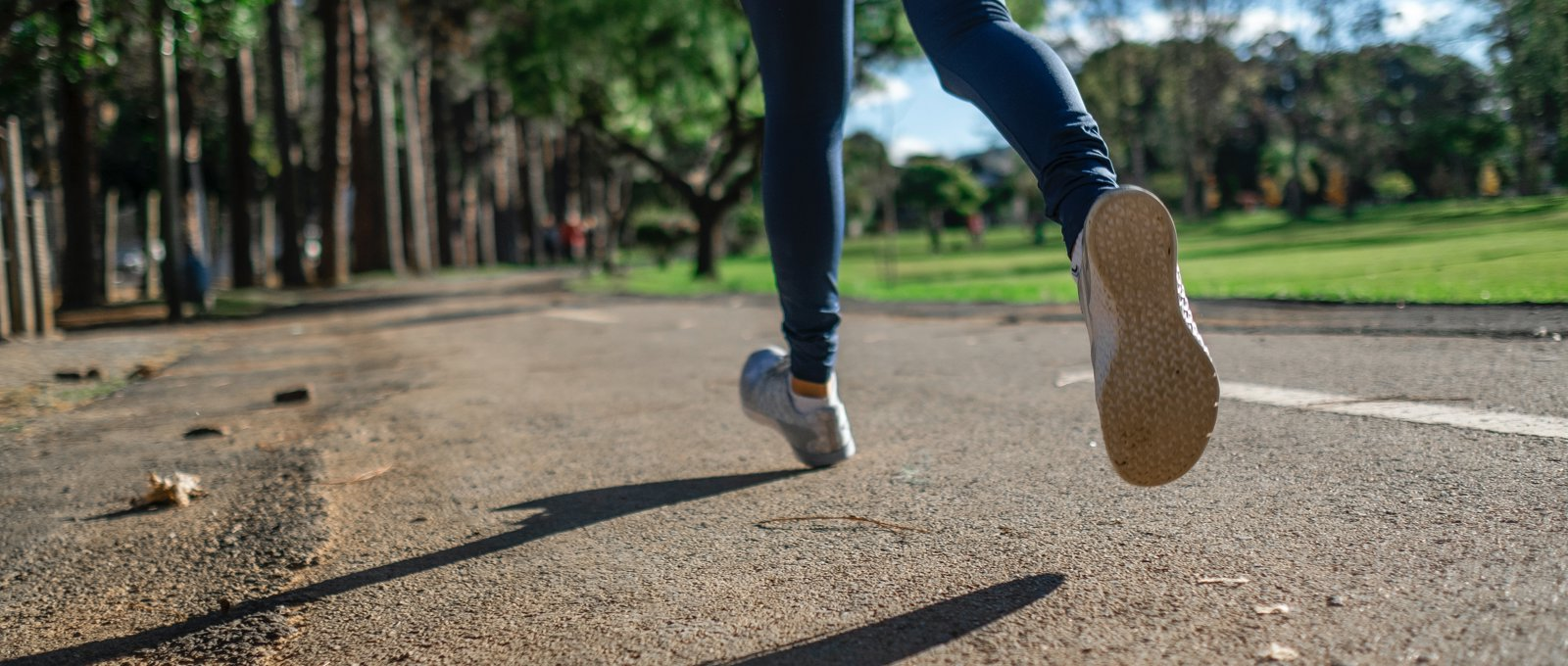 Close up photo of a woman's lower legs and feet taken as she jogs along a pathway in a park