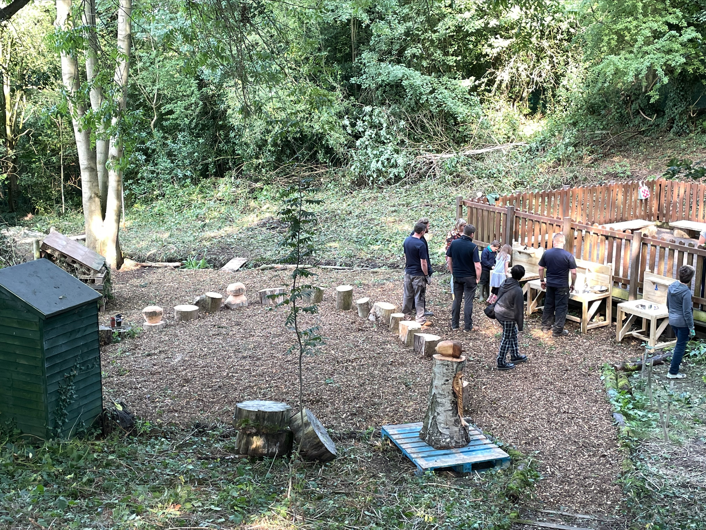 Photo of various team members from Futures working outdoors in a small woodland area at Lons infant School. There are various new wooden constructions in the photo.