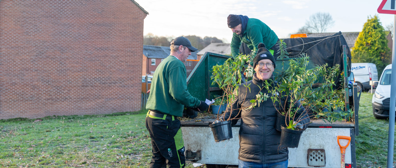 Photo of a Futures employee holding two plants and smiling at the camera as he helps to unload a truck