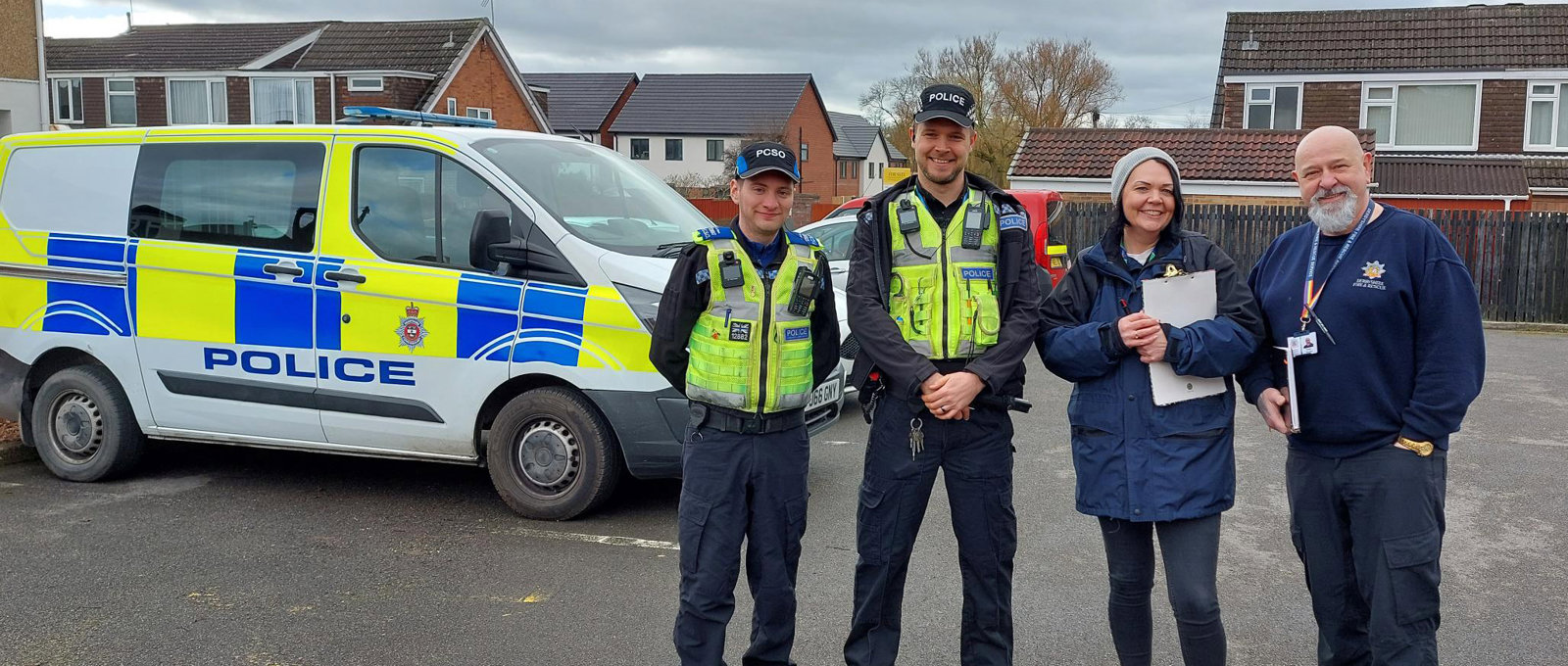 Photo of two Futures team members with two police officers, standing near some Futures homes with a police car in the background