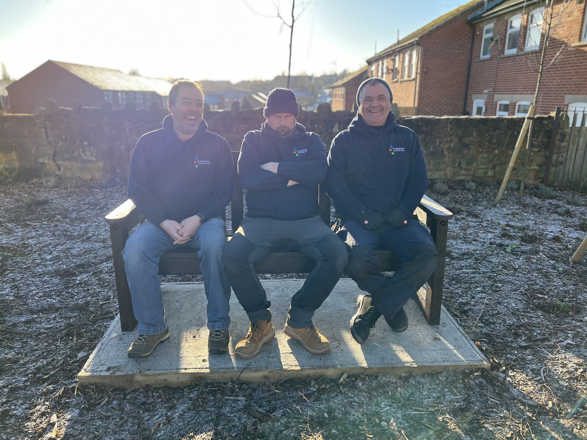 Photograph of three men who work for Futures smiling and sitting on an outdoor bench on a frosty but sunny day