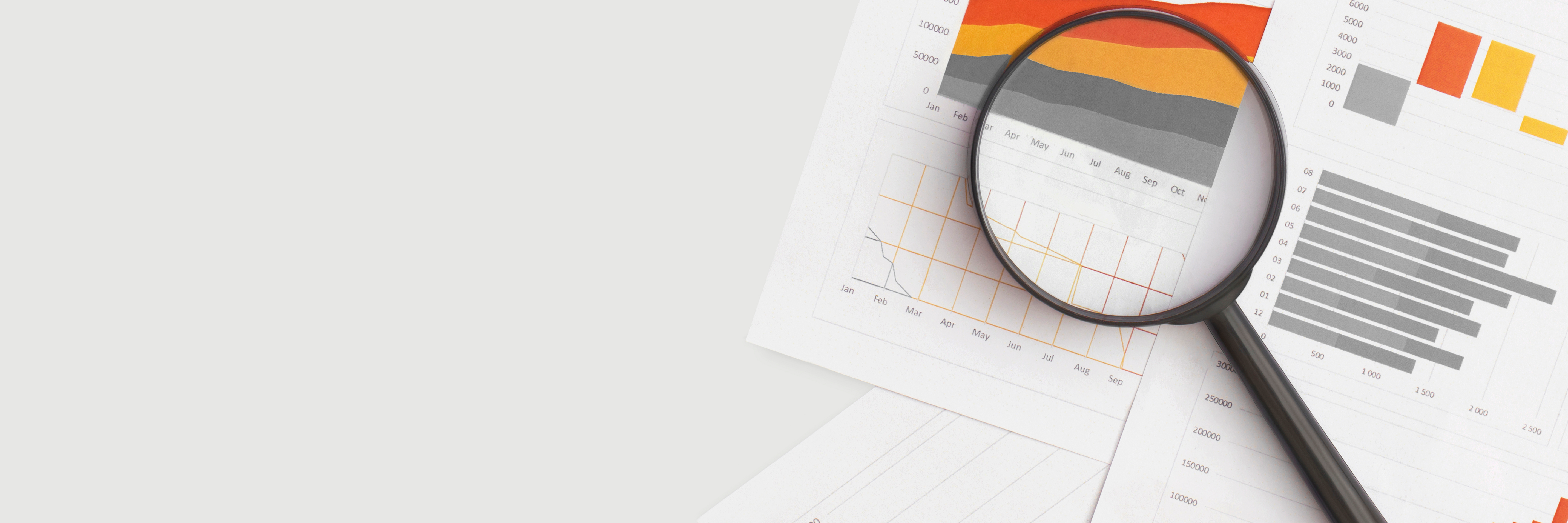 Photo of sheets of paper covered in graphs and charts on a white surface with a magnifying glass lying across them
