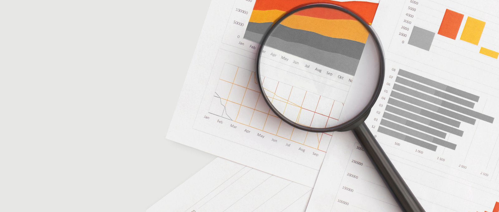 Photo of sheets of paper covered in graphs and charts on a white surface with a magnifying glass lying across them