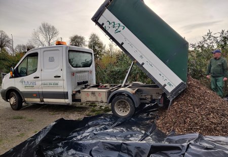 Photograph of an open back truck unloading a pile of tree bark chippings onto the ground