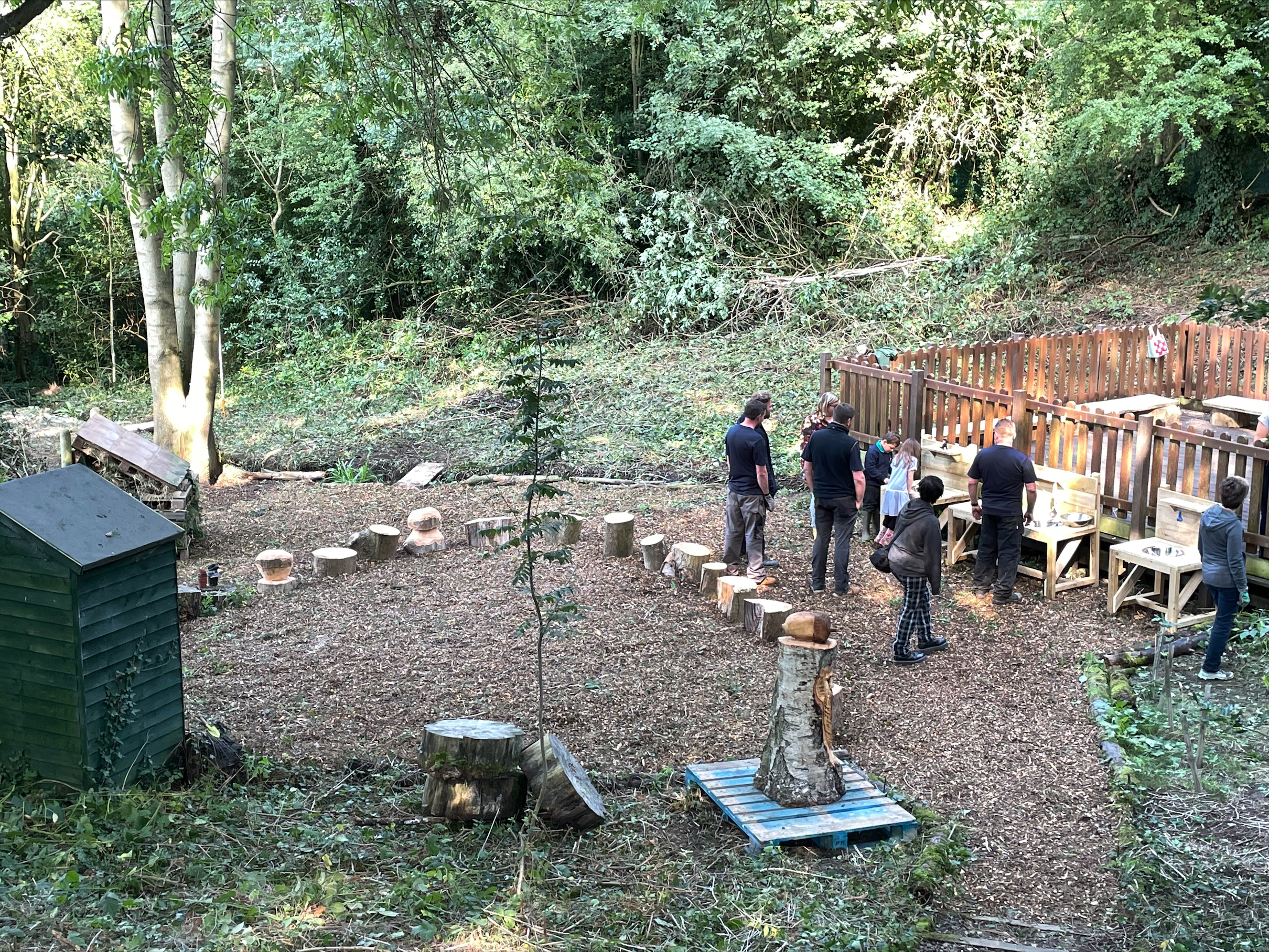 Photo of various team members from Futures working outdoors in a small woodland area at Lons infant School. There are various new wooden constructions in the photo.
