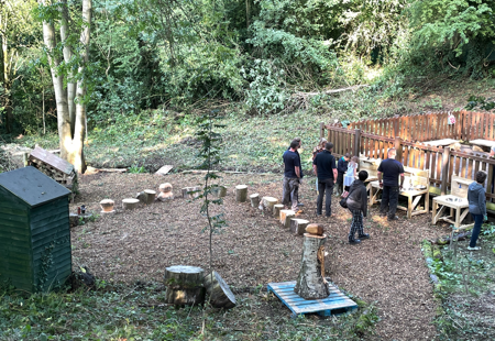 Photo of various team members from Futures working outdoors in a small woodland area at Lons infant School. There are various new wooden constructions in the photo.