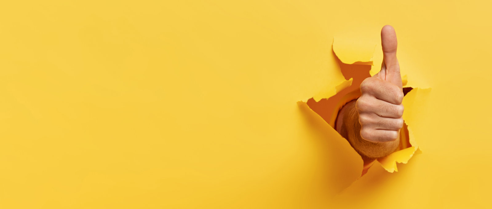 Photo of a hand with the thumb pointing up in a positive gesture that looks like it has been pushed through the yellow background
