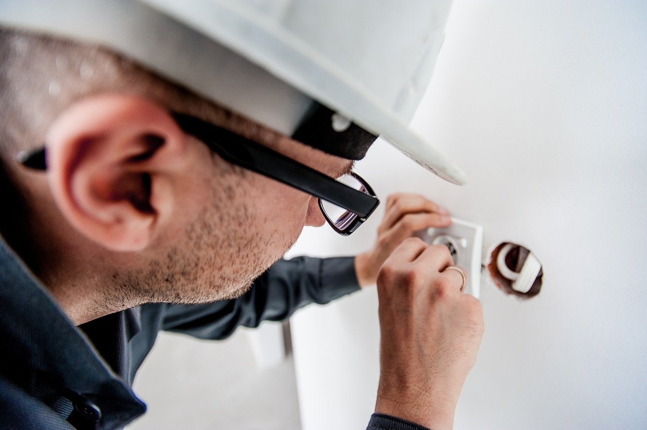 Close up photo of a man in a white hard hat installing an electrical socket in a wall