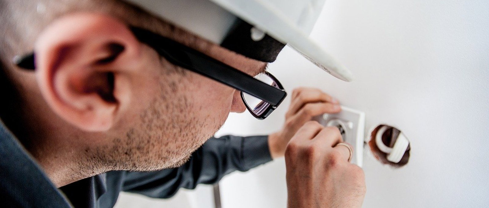 Close up photo of a man in a white hard hat installing an electrical socket in a wall