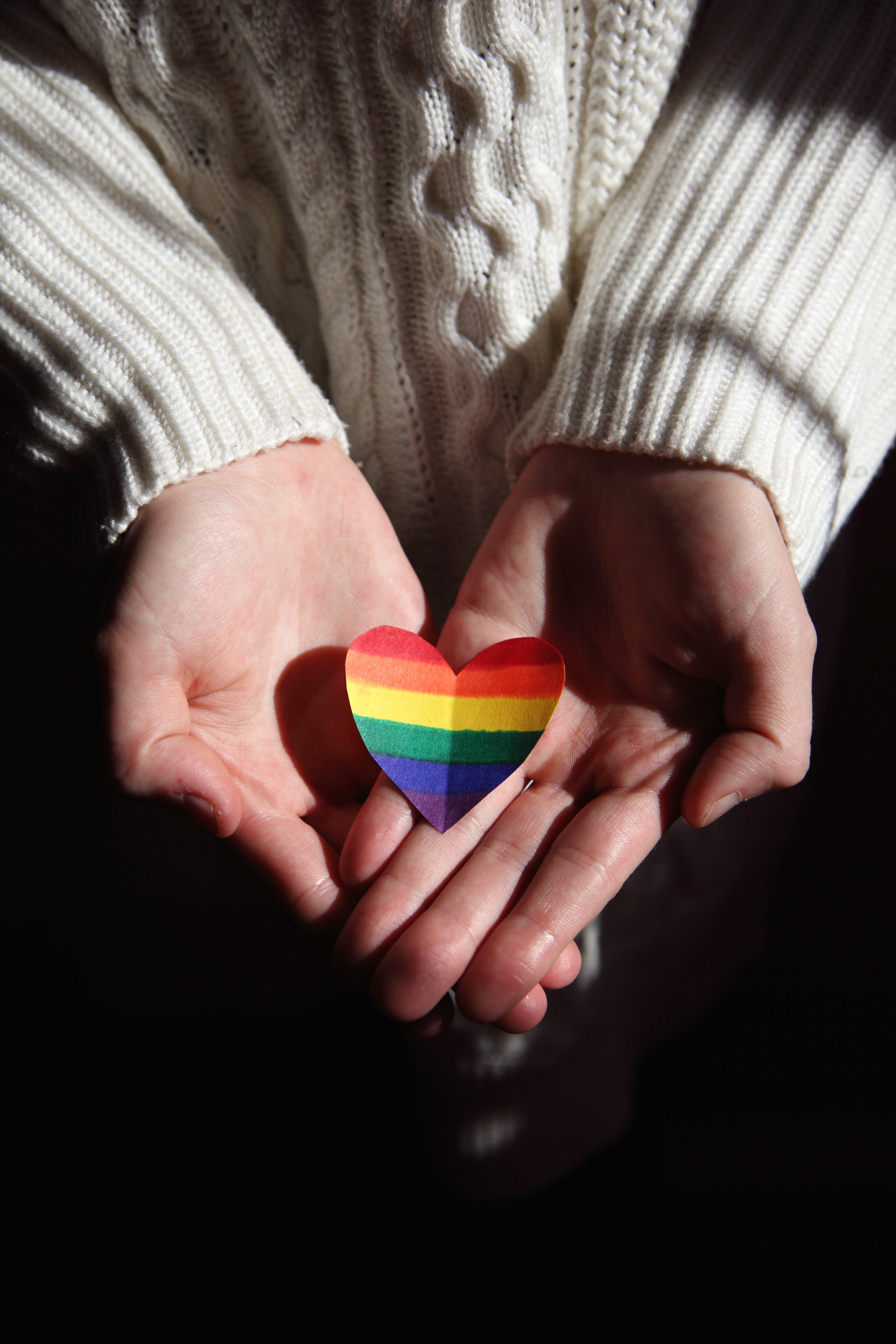 Close up photo of someone holding a cutout heart shape in rainbow colours in their outstretched, cupped hands