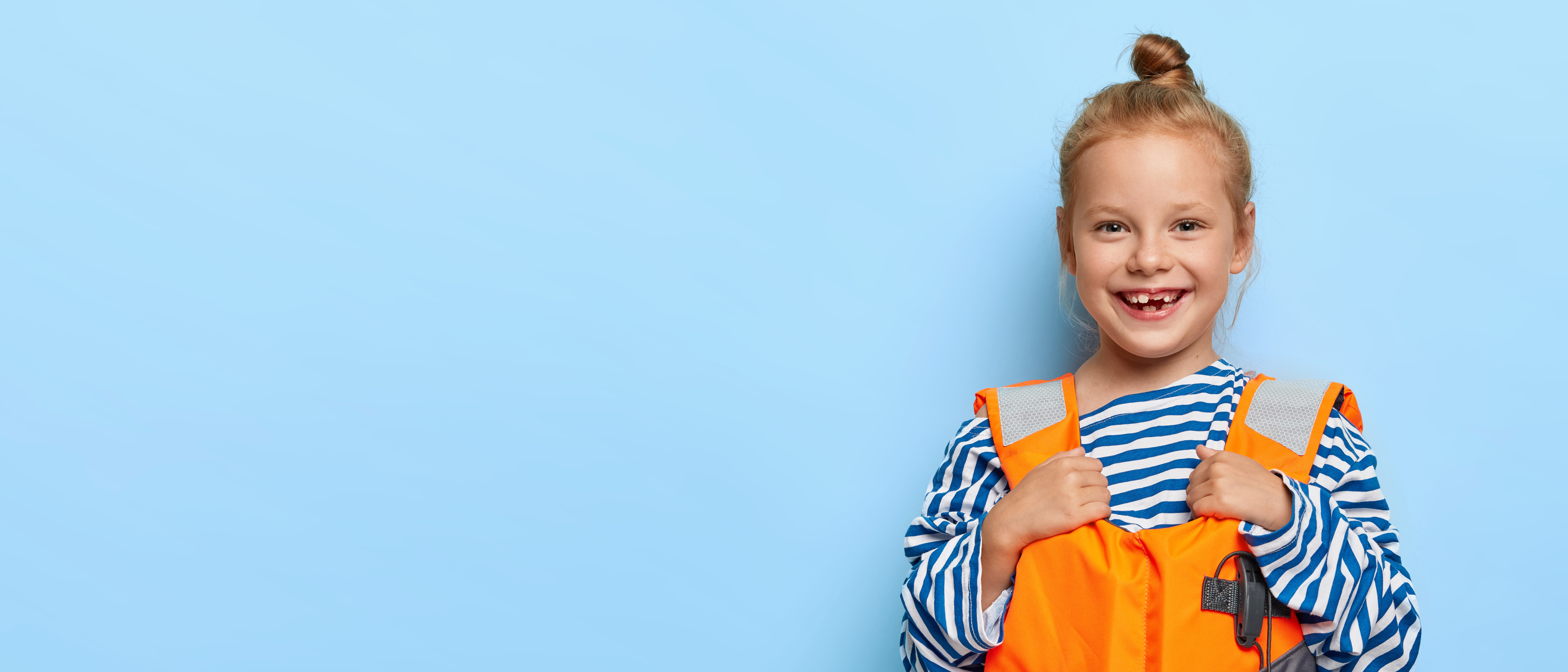 Photo of a smiling young girl wearing an orange and reflective lifejacket - standing in front of a blue background