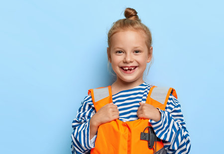 Photo of a smiling young girl wearing an orange and reflective lifejacket - standing in front of a blue background