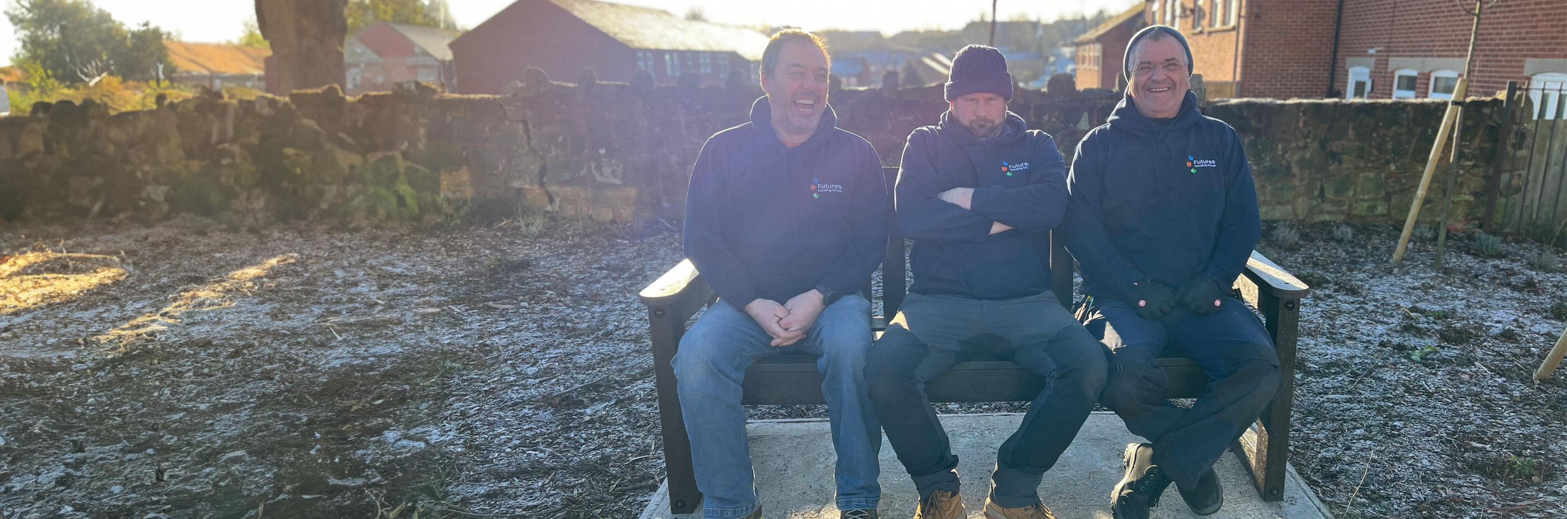 Photograph of three men who work for Futures smiling and sitting on an outdoor bench on a frosty but sunny day