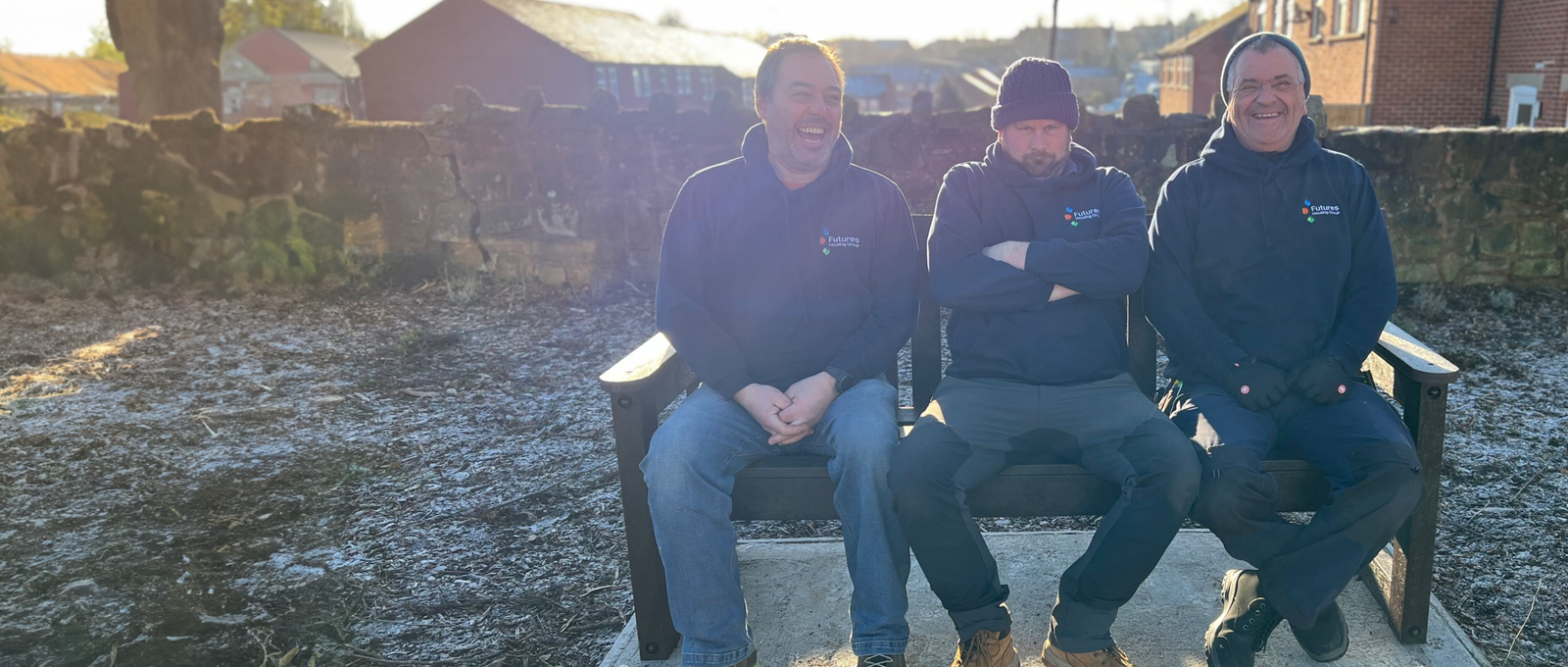 Photograph of three men who work for Futures smiling and sitting on an outdoor bench on a frosty but sunny day