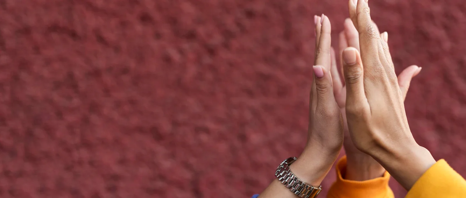 Close-up photo of three women's hands coming together in a high-five with a textured reddish wall in the background